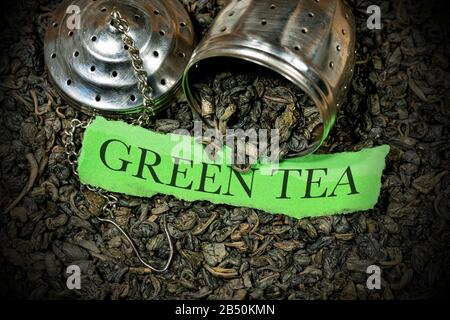 Nahaufnahme vieler getrockneter Blätter aus grünem Schießpulvertee mit Stahlsieb und einem Stück Papier mit Text Green Tea Stockfoto