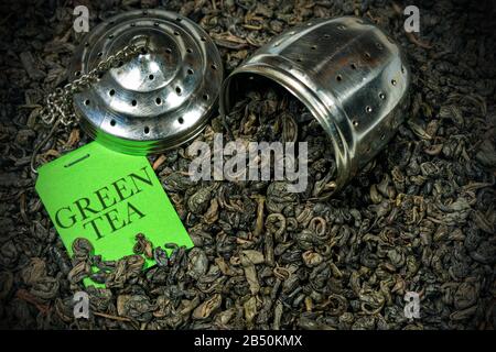 Nahaufnahme vieler getrockneter Blätter aus grünem Schießpulvertee mit Stahlsieb und grünem Etikett mit Text Green Tea Stockfoto