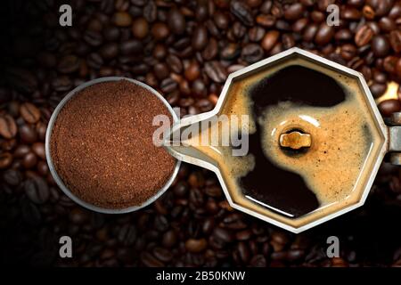 Nahaufnahme einer offenen italienischen Kaffeemaschine mit gemahlenem Kaffee in einem Metallfilter, auf vielen gebratenen Kaffeebohnen, Draufsicht Stockfoto