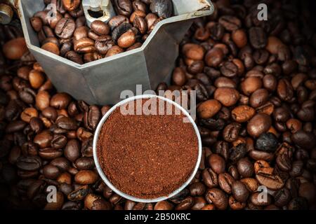 Nahaufnahme einer offenen italienischen Kaffeemaschine mit gemahlenem Kaffee im Metallfilter, auf vielen gebratenen Kaffeebohnen Stockfoto