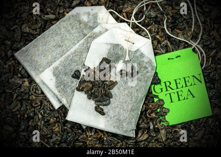 Nahaufnahme von drei grünen Teebeuteln, Gunpowder Tea, mit Etikett auf vielen getrockneten Blättern zur Zubereitung eines heißen Getränks Stockfoto