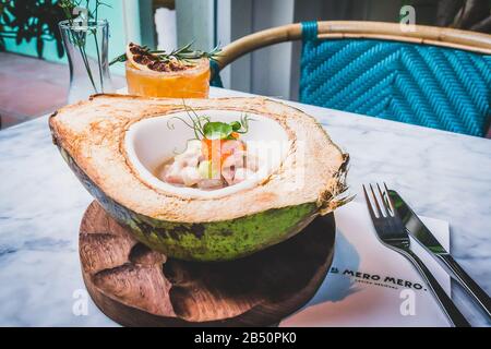 Hamachi und Kokosnuss Ceviche Hamachi auf einer frischen, grünen Kokosnuss, Hibiskusblütenmilch, Forellenrogen und Avocado-Püree und Blut Orange Margarita Stockfoto
