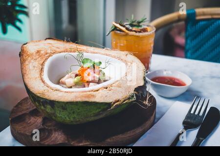 Hamachi und Kokosnuss Ceviche Hamachi auf einer frischen, grünen Kokosnuss, Hibiskusblütenmilch, Forellenrogen und Avocado-Püree und Blut Orange Margarita Stockfoto