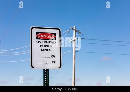 Straßenschild Warnung bei Gefahr von Oberleitungen. Elektrische Übertragungsleitungen und Pole im Hintergrund Stockfoto