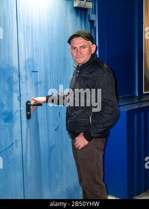 Ein Mann in einer Baseballmütze öffnet nachts ein Türschloss. Hintergrundbild für Personen. Vatertag. Platz für Text. Diebstahl. Das Verbrechen Stockfoto