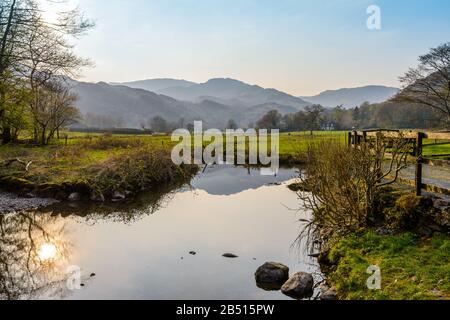 Im April spiegelte sich die untergehende Sonne in River Rothay vor dem Dorf Grasmere, Lake District National Park, Cumbria, England, Großbritannien, wider. Stockfoto