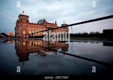 Berlin, Deutschland. März 2020. Das Gebäude des Reichstags glänzt im Abendlicht, die Kulisse spiegelt sich in einer Pfütze wider. Credit: Christoph Soeder / dpa / Alamy Live News Stockfoto