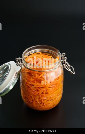 500 Gramm würziger koreanischer Karottensalat mit Öl, Knoblauch und schwarzem Pfeffer im Glasbecher. Nachhaltige Verpackung, schwarzer Hintergrund, hohe Auflösung Stockfoto