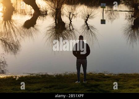 Ein junger Mann beobachtet die Überschwemmung des Flusses Cherwell, der einen Pub-Garten in Oxford nach starkem Regen unzugänglich macht Stockfoto