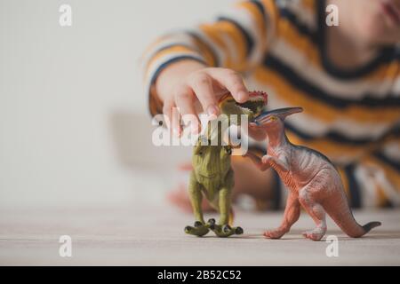 Details des Kindes zu Hause, das mit Dinosauriern spielt. Differentieller Fokus weißer Hintergrund. Kindheitskonzept. Stockfoto