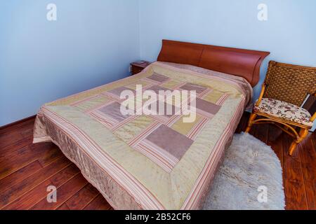 Ein großes Schlafzimmer mit Mahagoni, Korbstühlen und einem eleganten Schminktisch mit einem halbkreisförmigen Spiegel. Das Bett hat eine beige Decke in Quadraten. Stockfoto