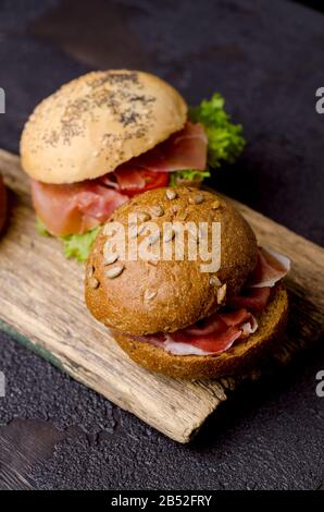 Knuspriger Burger mit Schinken in Scheiben auf einem Vintage-Holzschneidebrett. Dunkles, stimmungsvolles Speisefoto, gut für Bar-Menüs und Poster. Stockfoto