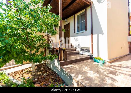 Vorhalle, Stufen und Eingang zum Haus im Hinterhof des Hauses. Vordach über dem Eingang. Schuhe auf der Veranda. Hinterhof mit Bäumen. Sonniger Tag Stockfoto