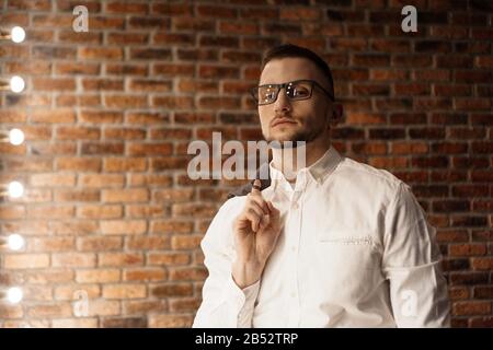 Gutaussehender Mann in weißem Hemd mit Brille, die in der Nähe der roten Ziegelwand steht Stockfoto