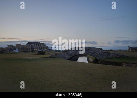 ST ANDREWS, SCHOTTLAND - 2/3/2020 - Die Swilcan Bridge auf dem Alten Kurs, mit dem Alten Kurhotel im Hintergrund, in der Dämmerung Stockfoto