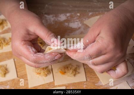 Eine Frau sculpt Knödel und Ravioli aus Kneten und Kohl. Sperrholzschneidplatte, Holzmehlsieb und Walzstift aus Holz - Werkzeuge für Stockfoto