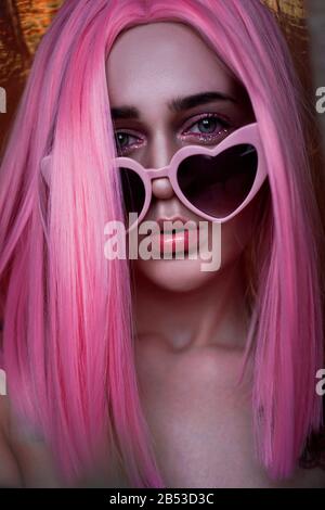 Porträt des Teenager-Modells mit rosafarbenem Haar. Funky Teenager mit farbigem Perücke und modischer Brille. Vertikales Foto - gutes Format für Geschichten Stockfoto