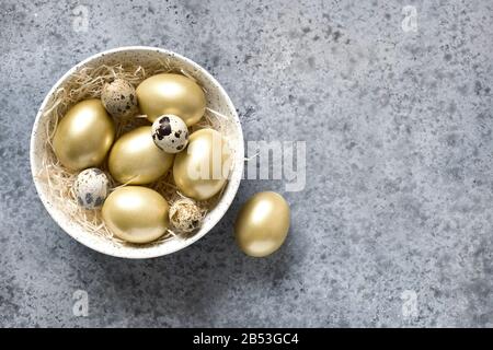 Ostergoldenes Hühnerei in Schüssel auf grauem Steingrund. Ansicht von oben. Kopierbereich. Stockfoto