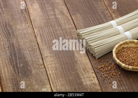 Gebündelte getrocknete Soba (Nudeln mit japanischem Buchweizen) und Buchweizensamen auf Holzgrund Stockfoto