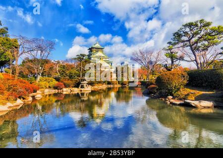 Kleiner Teich im traditionellen japanischen Garten des öffentlichen Parks in der Stadt Osaka an einem sonnigen Tag mit Reflexion von Bäumen und Türmen.