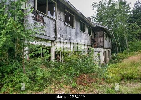 Eine verlassene Residenz in der Geisterstadt Ocean Falls, British Columbia, mit zerbrochenen Fenstern, einem abblätternden äußeren und dem Wald, der darauf eindringen kann. Stockfoto