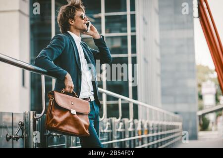 Junger Mann in einer sute, der draußen steht und auf dem Handy spricht und lächelt Stockfoto