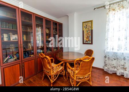 Hausbibliothek. Großer Bücherregal mit Büchertisch, Korbtisch und vier Stühlen. Holzparkett. Stockfoto