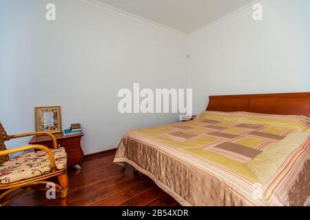 Ein großes Schlafzimmer mit Mahagoni, Korbstühlen und einem eleganten Schminktisch mit einem halbkreisförmigen Spiegel. Das Bett hat eine beige Decke in Quadraten. Stockfoto