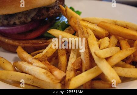 Lecker aussehender Hamburger auf einem Bun mit würzigen pommes frites auf einem Teller Stockfoto