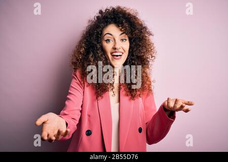 Junge schöne Geschäftsfrau mit lockigen Haaren und durchstechenden tragen elegante Jacke lächelnd fröhlich mit Händen, die Hilfe und Akzeptanz geben. Stockfoto