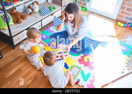 Schöne Lehrer und Kleinkinder spielen rund um viele Spielsachen im Kindergarten Stockfoto