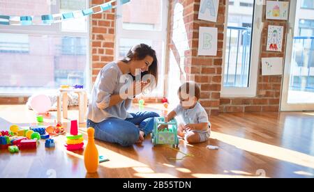 Schöne Lehrer und Kleinkind spielen um viele Spielsachen im Kindergarten Stockfoto