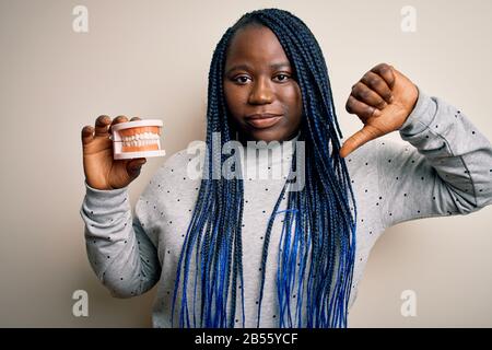 afroamerikanische Frau in Plus-Größe mit Zähnen aus Kunststoff über weißem Hintergrund mit verärgertem Gesicht, negatives Zeichen, das mit den Daumen nicht zu sehen ist Stockfoto