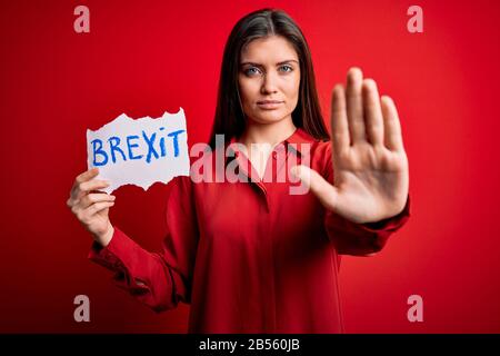 Junge schöne Frau mit blauen Augen, die Papier mit brexit Nachricht über rotem Hintergrund hält, mit offener Hand, die Stoppschild mit ernstem und selbstbewusem e macht Stockfoto