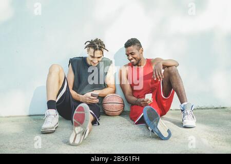 Junge, fröhliche Korbballspieler, die mit dem Smartphone im Freien Spaß haben - Beste Sportfreunde teilen Freizeit mit neuer Trendtechnologie - Technologie Stockfoto