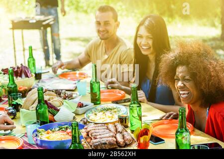 Gruppe verschiedener Kulturschaffende picknick-bbq-Mittagessen im Freien im Garten - Fröhliche Freunde, die Spaß am Grillen haben, Fleisch essen und Bier im Summ toben Stockfoto