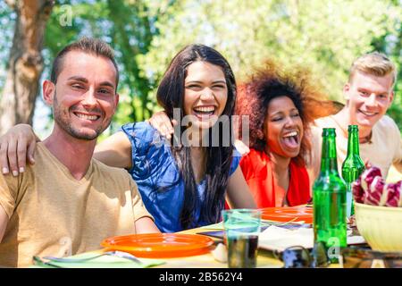 Multirassische Gruppe von Freunden, die im Freien im Park essen und grillen, Sommermahlzeit feiern - Junge Leute haben Spaß im Park - Konzentrieren sich auf den linken Kerl - Glück Stockfoto