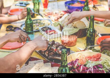 Eine Gruppe von Freunden, die auf der Grillparty im Freien in der Natur zu Abend essen - Nahaufnahme von Leuten, die Bier beim picknick-grillmenü essen und trinken - Freundschaft, summe Stockfoto