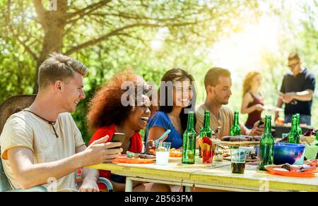 Fröhliche Freunde, die Bier toben und im Freien grillen, mit Sonnenschein - Junge Leute, die Spaß an der grillparty haben - Freundschaft, Sommer, Spaß und Abendessen Stockfoto