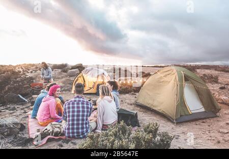 Fröhliche Freunde, die bei Sonnenuntergang in der Wüste ein Picknick machen - Junge Leute haben Spaß beim Abendessen - Reisen, Abenteuer auf der Natur, va Stockfoto