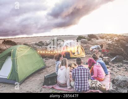 Fröhliche Freunde, die bei Sonnenuntergang in der Wüste ein Picknick machen - Junge Leute haben Spaß beim Abendessen - Reisen, Abenteuer auf Tour in der Natur, vac Stockfoto