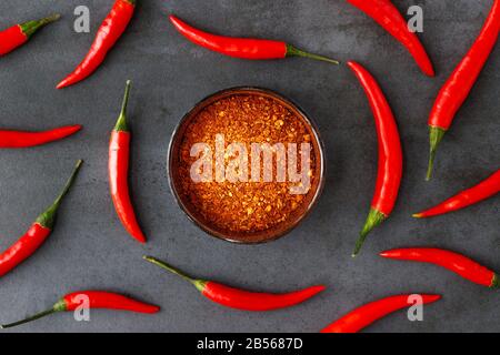 Flat Lay of Thai Red Fresh Hot Chili Paprika with Green tails and getrockneten roten Chili Flocken in Bowl on Black Stone Background. Lebensmittelmuster. Beliebter sp Stockfoto