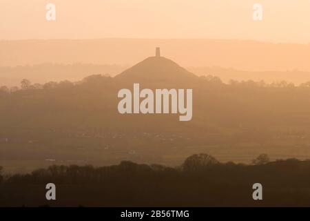 Glastonbury, Somerset, Großbritannien. März 2020. Wetter in Großbritannien. Glastonbury Tor, das im Dunst in der Ferne bei Sonnenuntergang von der Old Frome Road in der Nähe von Shepton Mallet in Somerset silhouettiert ist. Bildnachweis: Graham Hunt/Alamy Live News Stockfoto