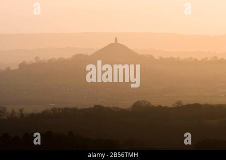 Glastonbury, Somerset, Großbritannien. März 2020. Wetter in Großbritannien. Glastonbury Tor, das im Dunst in der Ferne bei Sonnenuntergang von der Old Frome Road in der Nähe von Shepton Mallet in Somerset silhouettiert ist. Bildnachweis: Graham Hunt/Alamy Live News Stockfoto