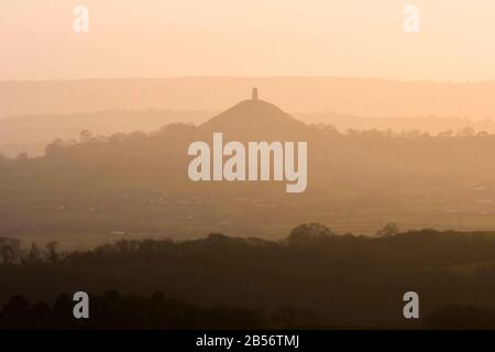 Glastonbury, Somerset, Großbritannien. März 2020. Wetter in Großbritannien. Glastonbury Tor, das im Dunst in der Ferne bei Sonnenuntergang von der Old Frome Road in der Nähe von Shepton Mallet in Somerset silhouettiert ist. Bildnachweis: Graham Hunt/Alamy Live News Stockfoto