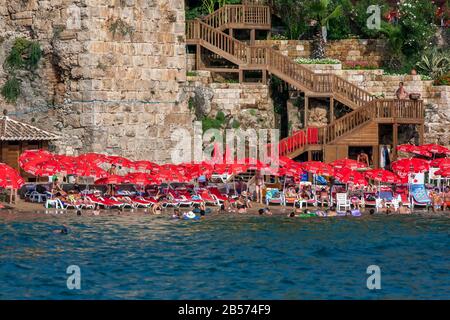 An einem heißen Sommertag genießen die Menschen das Baden im Mermerli Plaji neben den alten römischen Hafenmauern in Kaleici an der Antalya-Bucht in der Türkei. Stockfoto