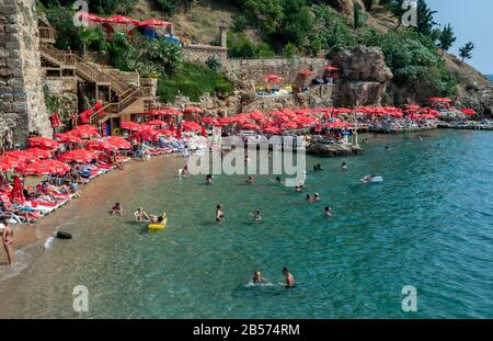 An einem heißen Sommertag genießen die Menschen das Baden im Mermerli Plaji neben den alten römischen Hafenmauern in Kaleici an der Antalya-Bucht in der Türkei. Stockfoto