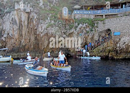Touristen in kleinen Booten warten auf die berühmte Blaue Grotte auf der Insel Capri. Die Fahrer ziehen Boote durch eine kleine Öffnung. Stockfoto