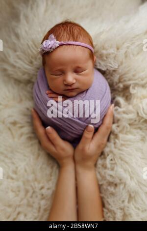Neugeborenes Babymädchen schläft in einer Kokonenpose (Kartoffeltasche) in den Armen seiner Mutter. Das Konzept der Sicherheit und des Glücks Stockfoto