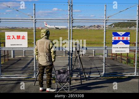 Unidentifizierter Mann, der ein Foto des Flugzeuges durch den Zaun am Flughafen Fukuoka gemacht hat Stockfoto